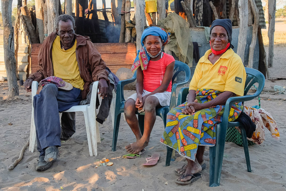 Anatercia sits with her grandfather and grandmother outside their home in Mozambique