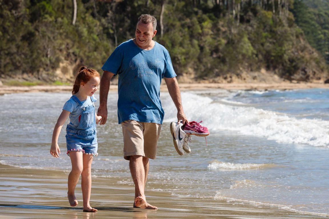 Father and daughter walking along the beach holding hands in Australia